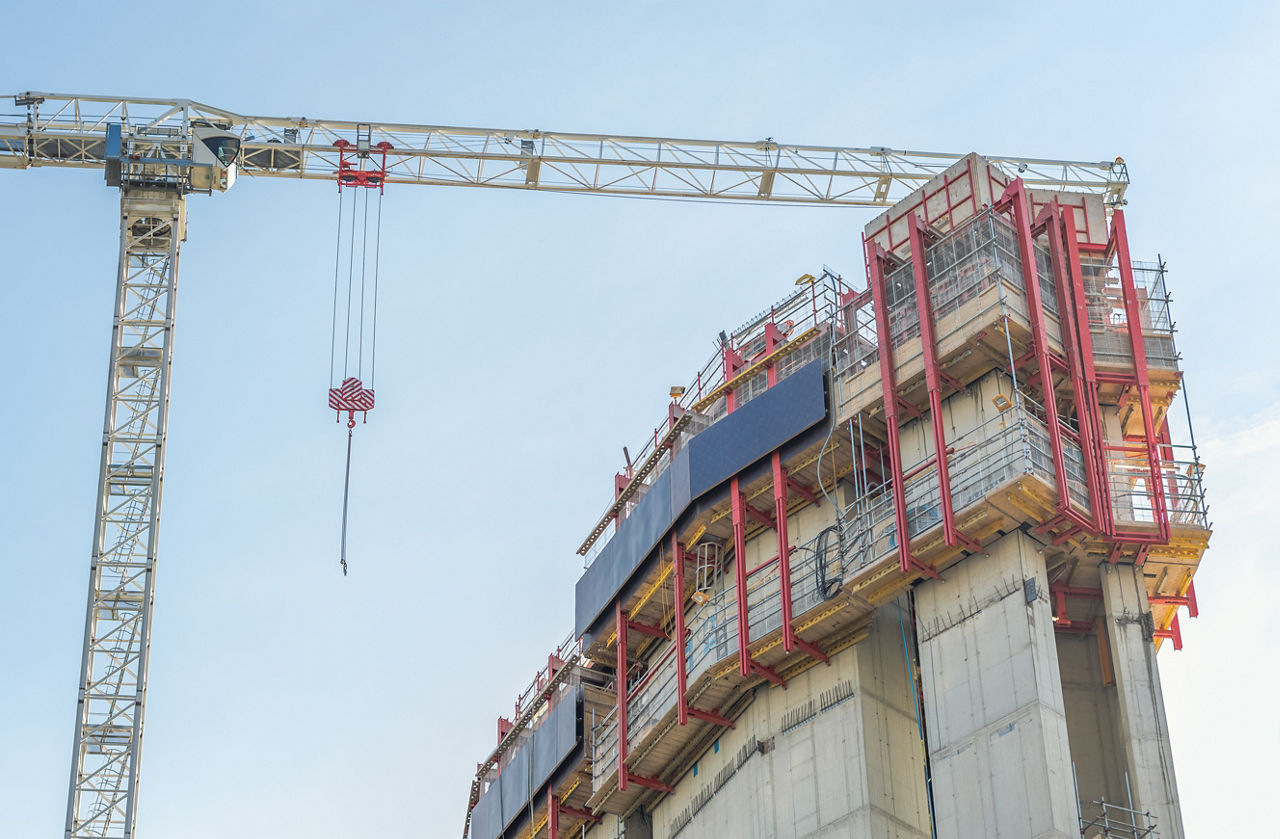 A construction site with a large crane and a partially built concrete structure equipped with red scaffolding and safety barriers in London